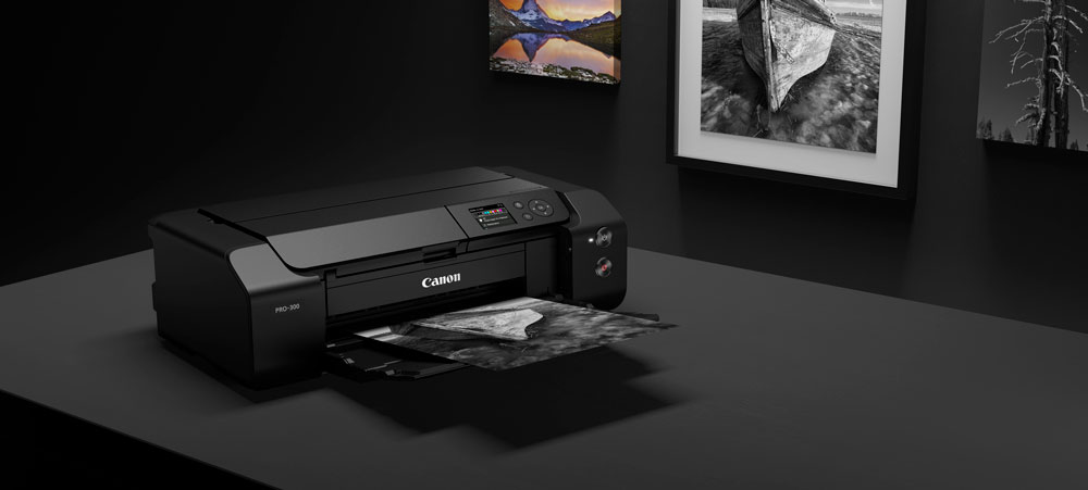 Canon PRO-300 printer on a black table with prints on the wall